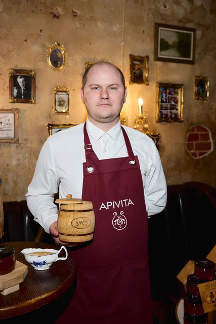 Участник встречи в фартуке APIVITA держит бочонок